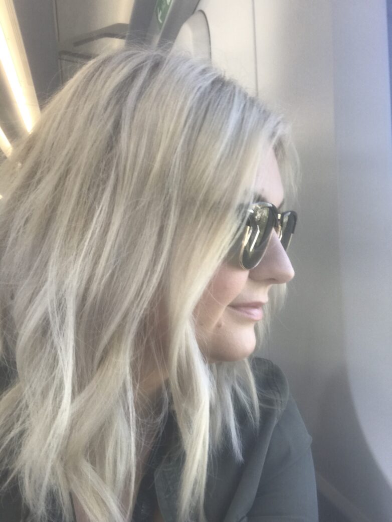woman with blond hair and sunglasses looking out window